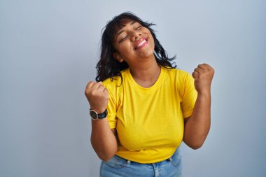 Mavi arka planda dikilen İspanyol kadın şaşkınlık ve şaşkınlık içinde kollarını kaldırarak ve gözlerini kapayarak başarıyı kutluyor. Kazanan konsept. 