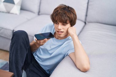 Young blond man talking on smartphone sitting on floor at home
