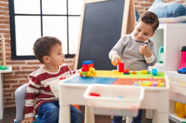 Two kids playing with construction blocks sitting on table at kindergarten