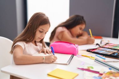 Two kids preschool students sitting on table drawing on paper at classroom