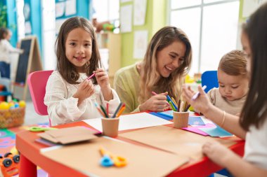 Teacher with boy and girl sitting on table drawing on paper at kindergarten
