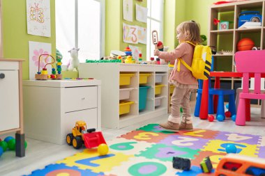 Adorable blonde girl smiling confident playing maraca at kindergarten