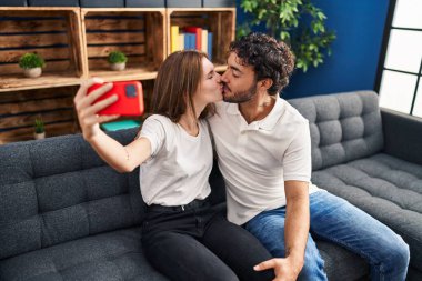 Erkek ve kadın öpüşüyor ve sarılıyorlar. Evdeki akıllı telefonun yanında selfie çekiyorlar.