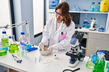 Laboratuvarda çalışan, bilim adamı üniforması giyen genç Latin kadın.