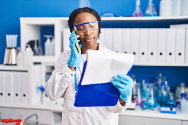 Bilim adamı üniforması giyen Afrikalı Amerikalı kadın akıllı telefon laboratuvarında konuşuyor.