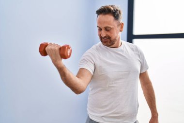 Spor merkezinde dambıl eğitimi alarak gülümseyen beyaz bir genç.