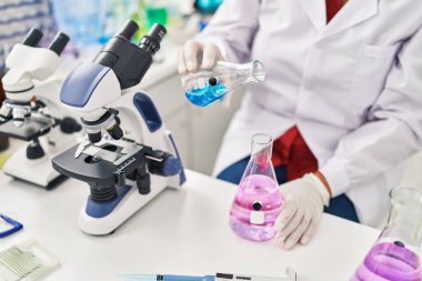 Middle age hispanic woman wearing scientist measuring liquid at laboratory