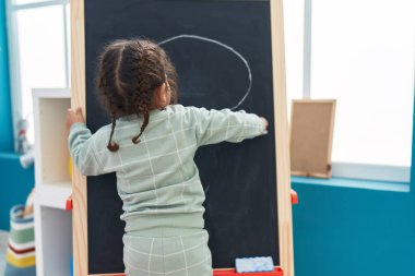 Anaokulunda tahtaya resim çizen sevimli İspanyol çocuk anaokulu öğrencisi.