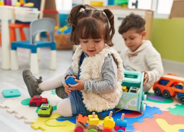 Brother and sister playing with cars toy sitting on floor at kindergarten