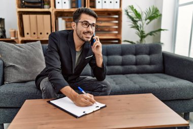 Young hispanic man having psychology session talking on the smartphone at clinic