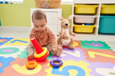 Adorable hispanic toddler playing with hoops toy sitting on floor at kindergarten
