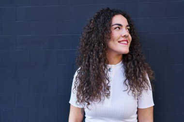 Genç, güzel İspanyol bir kadın, kendinden emin gülümsüyor ve izole edilmiş siyah bir arkaplanda yan tarafa bakıyor.