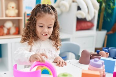 Sevimli sarışın çocuk anaokulundaki masada oyuncaklarla oynuyor.