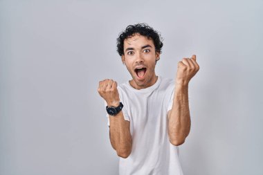 Hispanic man standing over isolated background celebrating crazy and amazed for success with arms raised and open eyes screaming excited. winner concept 