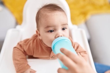 Tapılası İspanyol bebek evde şezlongda su içiyor.