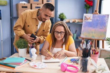 Man and woman artists drawing on notebook holding smartphone at art studio