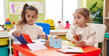 Two kids preschool students sitting on table drawing on paper at kindergarten