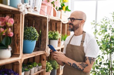 Çiçekçiye akıllı telefon kullanarak gülümseyen kel bir çiçekçi.