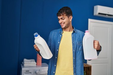 Çamaşır odasında çamaşır deterjanı şişeleriyle çamaşır yıkayan İspanyol genç adam.