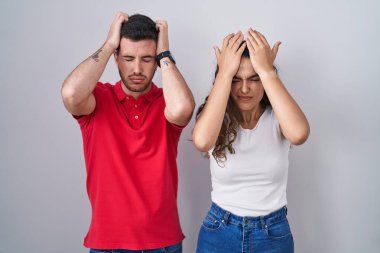 Young hispanic couple standing over isolated background suffering from headache desperate and stressed because pain and migraine. hands on head. 