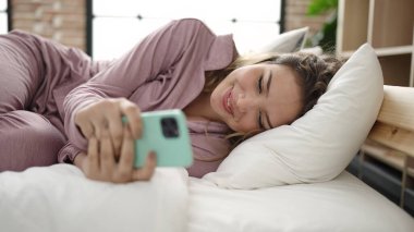 Yatakta uzanmış akıllı telefon kullanan genç, güzel İspanyol kadın.