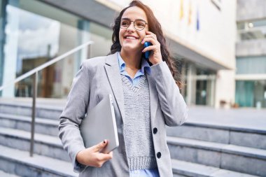 Genç İspanyol kadın yönetici caddede akıllı telefondan konuşuyor.