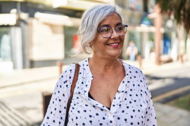 Orta yaşlı bir kadın sokakta kendine güvenerek gülümsüyor.