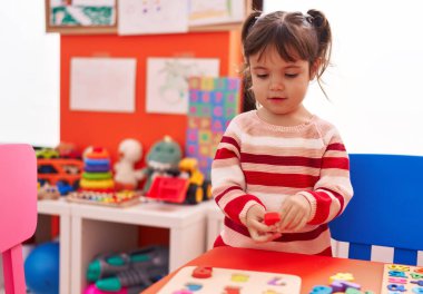 Adorable hispanic girl playing with maths puzzle game standing at kindergarten