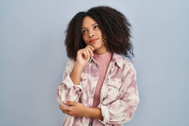 Young african american woman standing over blue background with hand on chin thinking about question, pensive expression. smiling with thoughtful face. doubt concept. 