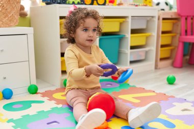 Adorable hispanic toddler playing with hoops toy sitting on floor at kindergarten