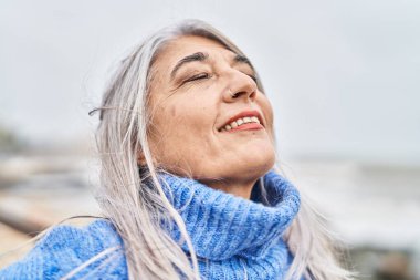Orta yaşlı, kır saçlı, gülümseyen, kendine güvenen bir kadın.