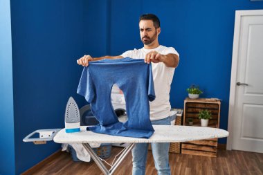 Sakallı, ütülü genç İspanyol adam çamaşırhanede yakılmış demir gömlekli şüpheci ve sinirli, sorun yüzünden üzgün. negatif kişi. 