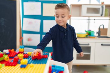 Adorable hispanic boy playing with construction blocks standing at kindergarten