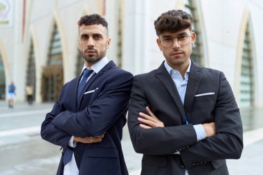 Two hispanic men business workers standing with arms crossed gesture at street