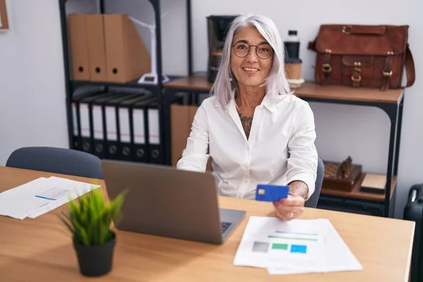 在办公室使用笔记本电脑和信用卡的中年灰发女商人 — 图库照片