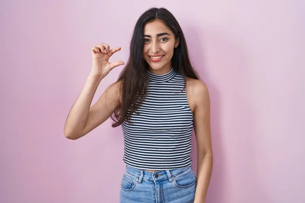 Young teenager girl wearing casual striped t shirt smiling and confident gesturing with hand doing small size sign with fingers looking and the camera. measure concept.