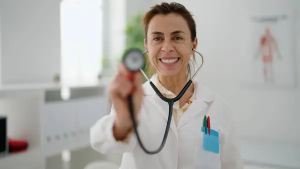 Mulher Hispânica Meia Idade Vestindo Uniforme Médico Segurando Estetoscópio Clínica — Fotografia de Stock