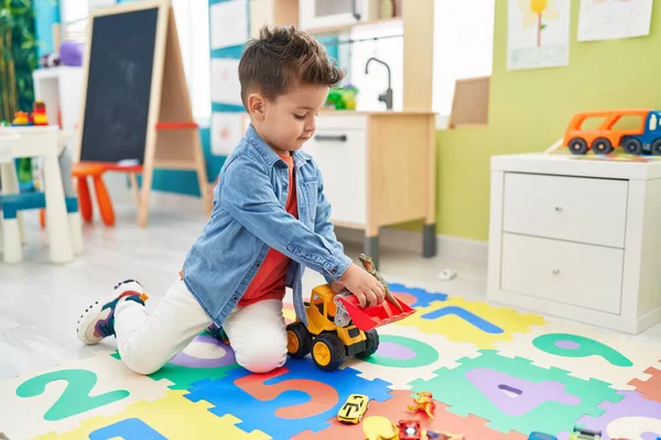 愛らしいヒスパニック幼児遊びとともにトラクターとディノおもちゃ座っています床に幼稚園 — ストック写真