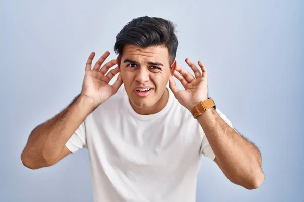 Латиноамериканец Стоящий Синем Фоне Пытающийся Услышать Обе Руки Жесте Уха — стоковое фото