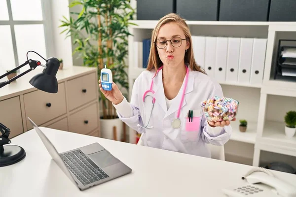 Young Blonde Doctor Woman Holding Glucometer Sweets Making Fish Face — ストック写真