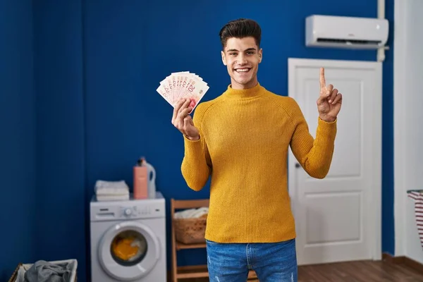 Young Hispanic Man Laundry Room Holding Shekels Smiling Idea Question — Stockfoto