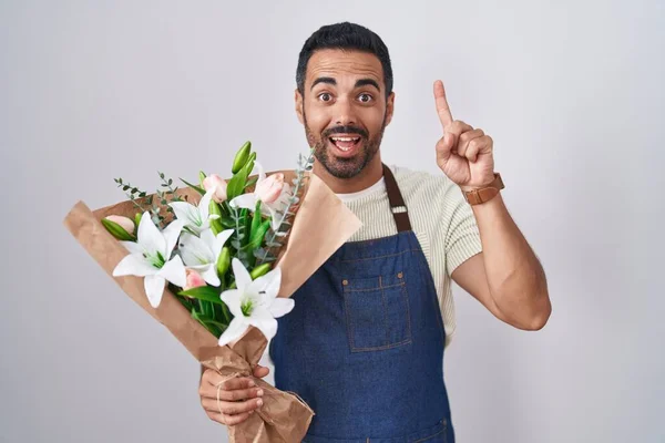 Hispanic man with beard working as florist smiling amazed and surprised and pointing up with fingers and raised arms.