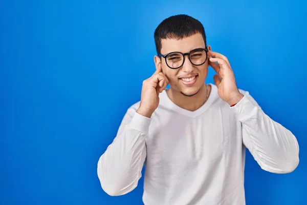 白いカジュアルなシャツを着た若いアラブ人男性と 大きな音楽のノイズのためにいらいらする表情で指で耳を覆う眼鏡 聴覚障害の概念 — ストック写真