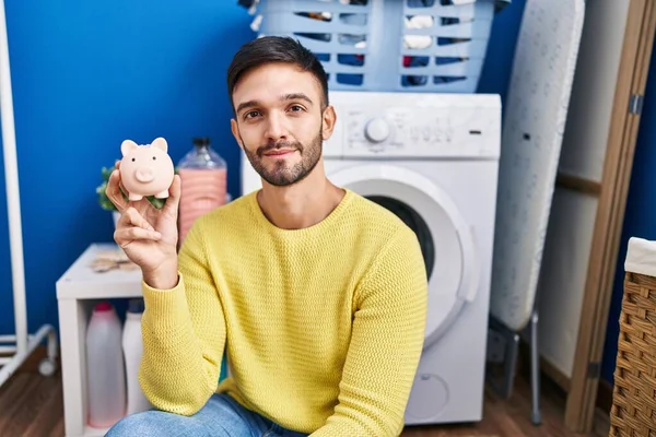 Hispanic Man Doing Laundry Holding Piggy Bank Thinking Attitude Sober — Stock Photo, Image