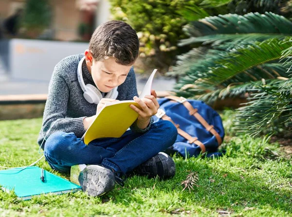 一个金发学生坐在公园的草地上看书 — 图库照片
