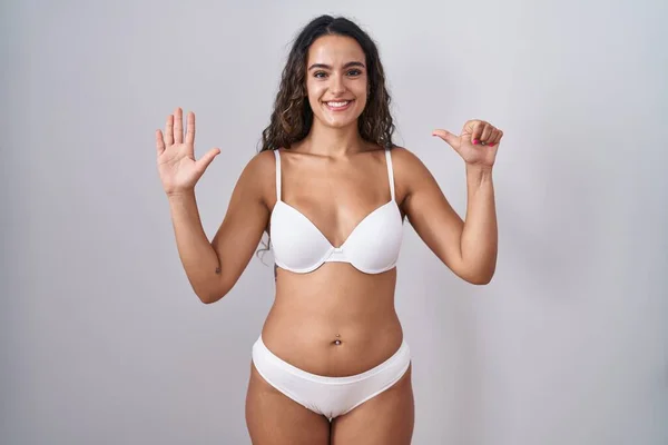Young hispanic woman wearing white lingerie showing and pointing up with fingers number six while smiling confident and happy.