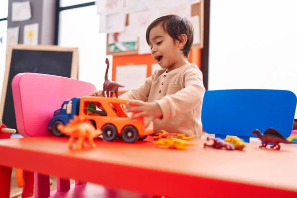 幼稚園に立っている車やディノのおもちゃで遊んでいる愛らしいヒスパニック系の男の子 — ストック写真