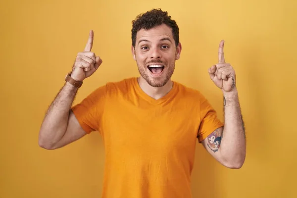 Young Hispanic Man Standing Yellow Background Smiling Amazed Surprised Pointing —  Fotos de Stock