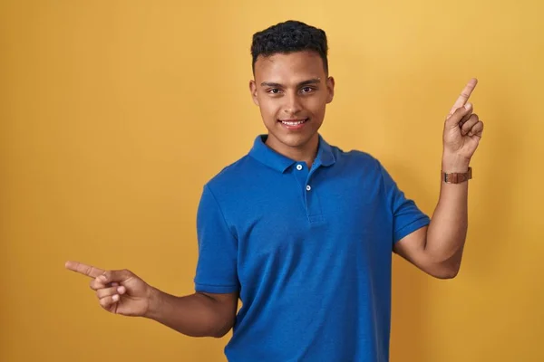 Mladý Hispánec Stojící Nad Žlutým Pozadím Sebevědomě Usmívá Ukazuje Prsty — Stock fotografie