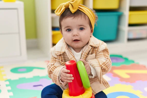 幼稚园里可爱的金发碧眼的幼儿抱着圈圈玩具坐在地板上 — 图库照片